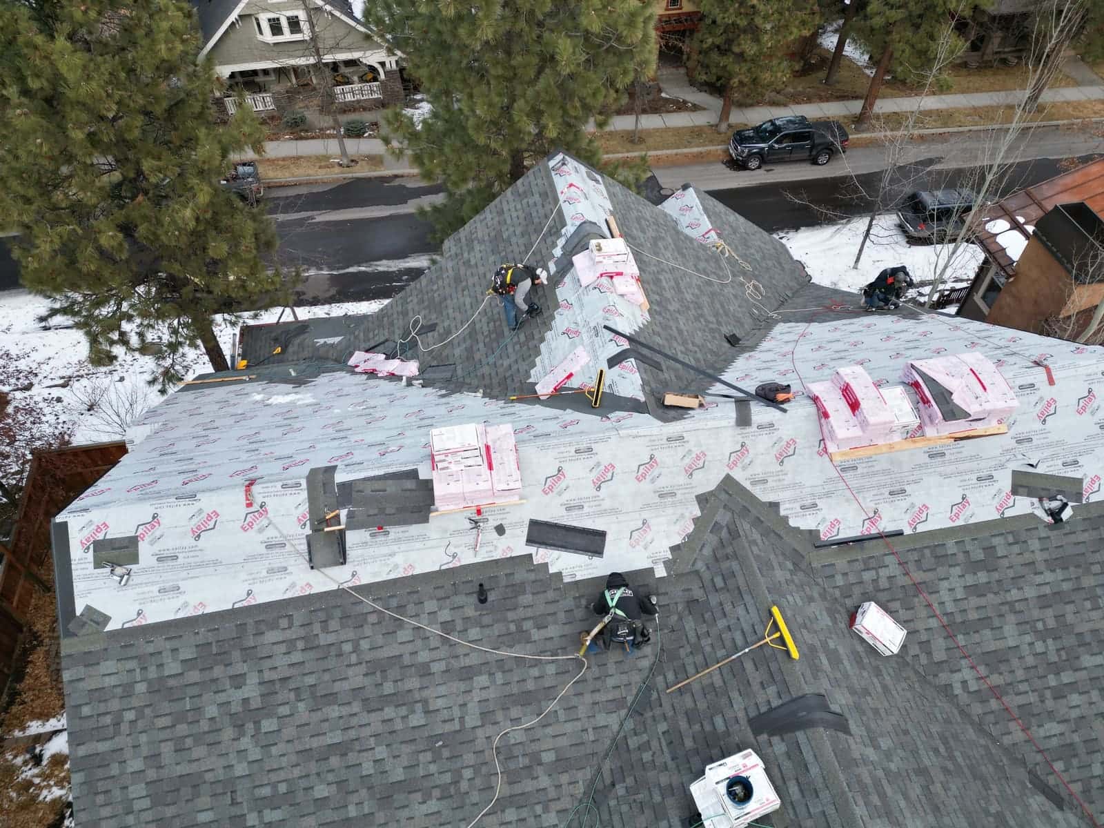 Greenlee crew laying synthetic underlayment and gray shingles on a Madras home in winter