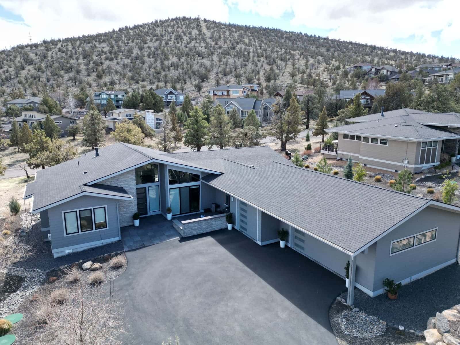 Gray shingle roof on a single-story modern Prineville home with a juniper hillside behind