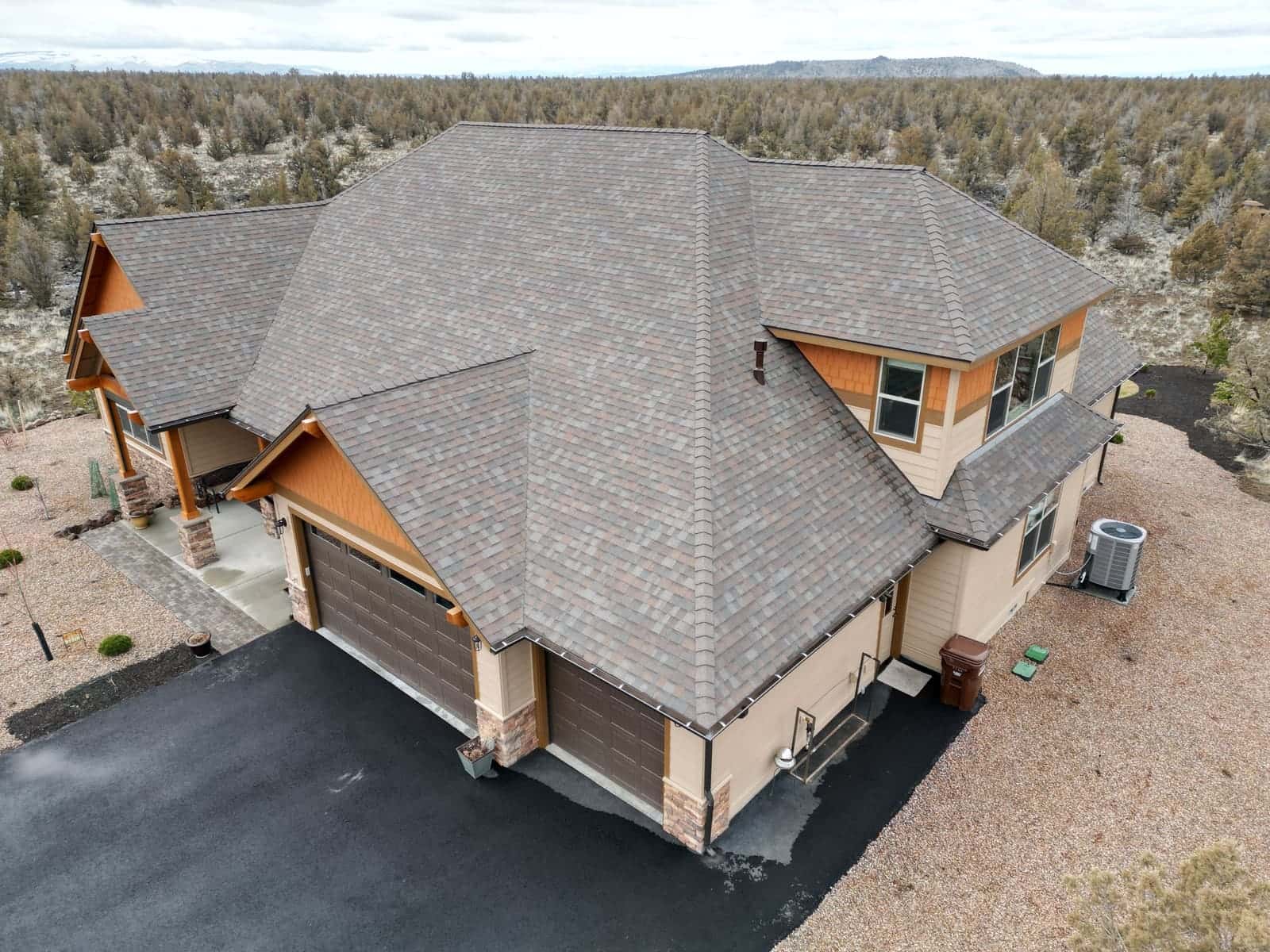 Blended brown and gray architectural shingles on a large Sisters home with juniper hills behind