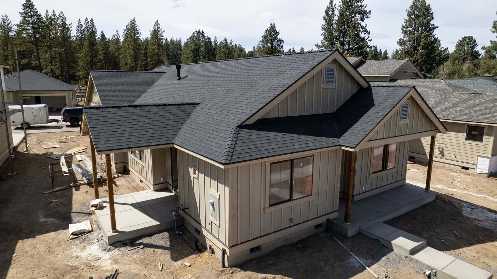 New board-and-batten home in Sunriver with a black architectural shingle roof, pines behind